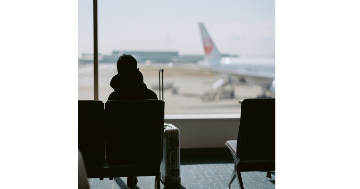 A person looking out an airport window at a departing plane, symbolizing the feeling of leaving Japan and reflecting on its pros and cons.